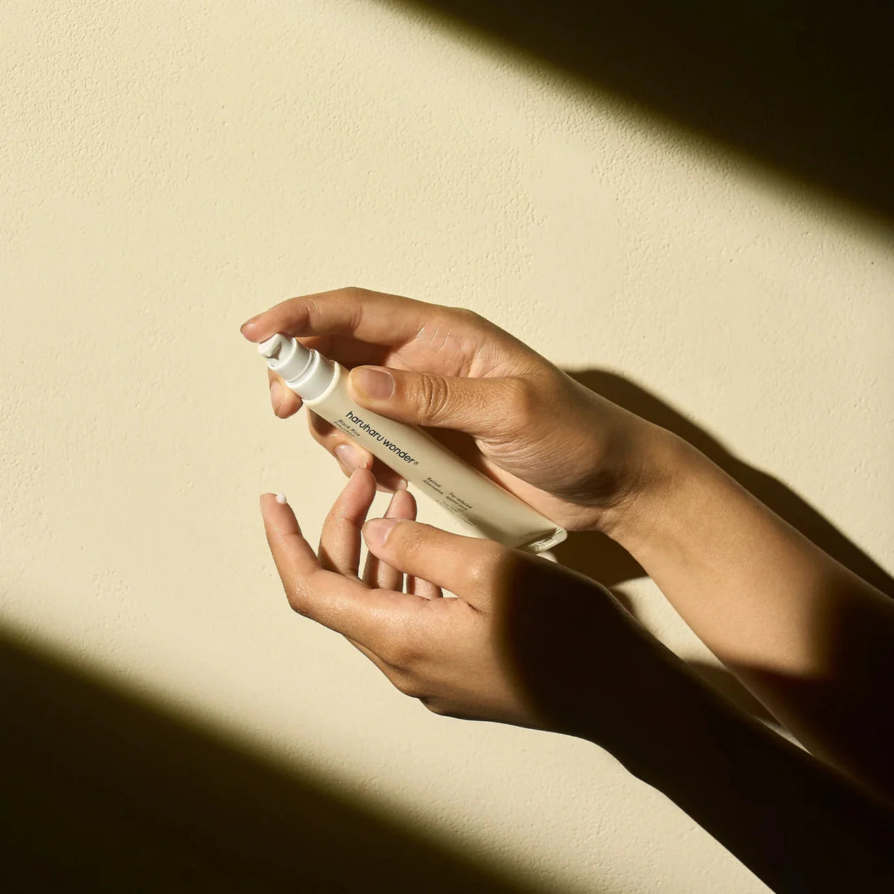 Hand holding a white spray bottle against a beige background