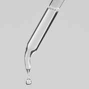 Glass dropper with clear liquid on a gray background
