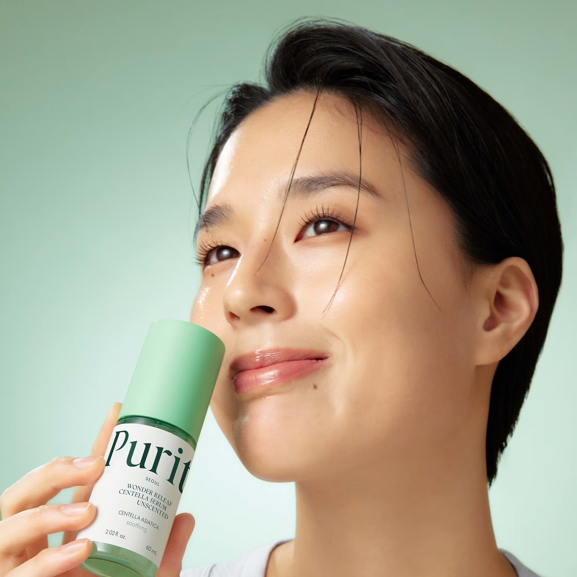 Woman holding a green skincare product with a light green background